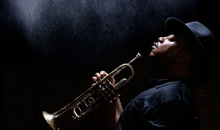 Nicholas Payton in profile holding a trumpet.