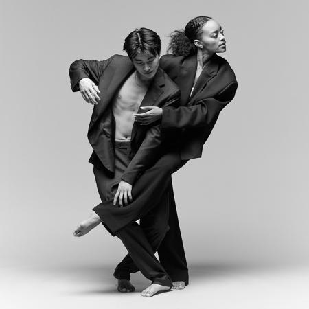 Two members of A.I.M by Kyle Abraham in dark suit jackets and pants in a black and white photo against a gray background