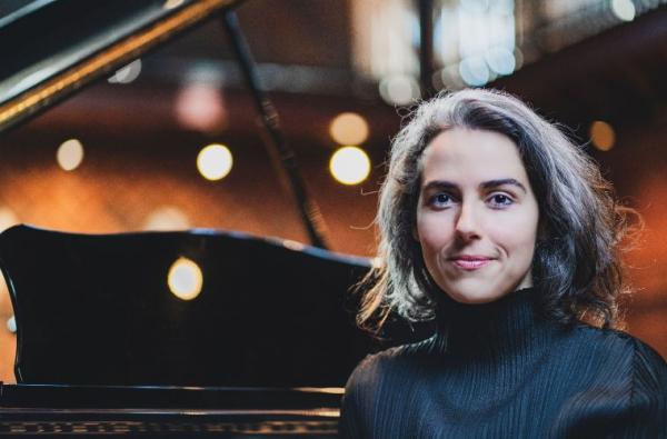 Clarice Assad sitting next to a grand piano