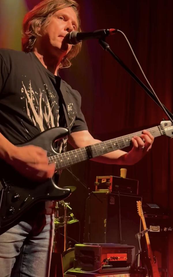Another member of the band playing electric guitar.
