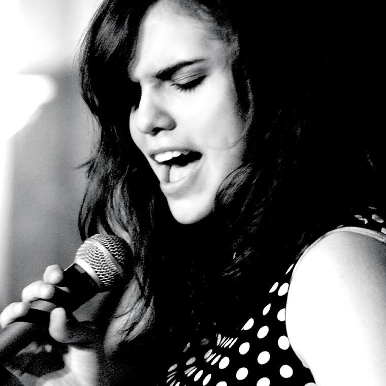 Julia Keefe in a spotted dress holding a microphone and singing